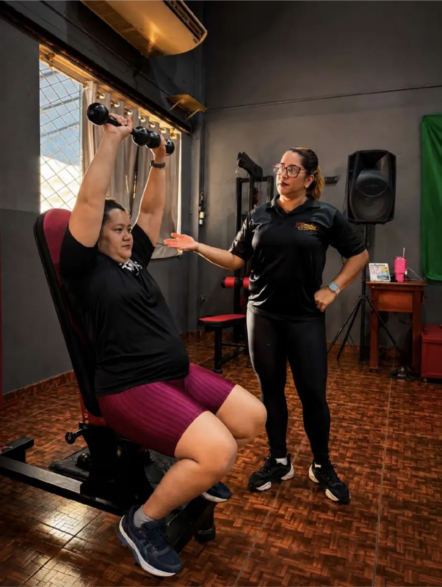 Professora acompanhando aluna durante exercício com halteres